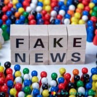 gestapelte Würfel mit der Aufschrift FAKE NEWS mit sympolischen Spielfiguren herum