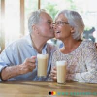 Rentnerehepaar küsst sich mit Kaffee in der Hand