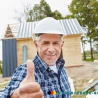 Ein älterer Mann mit Schutzhelm streckt den Daumen hoch.